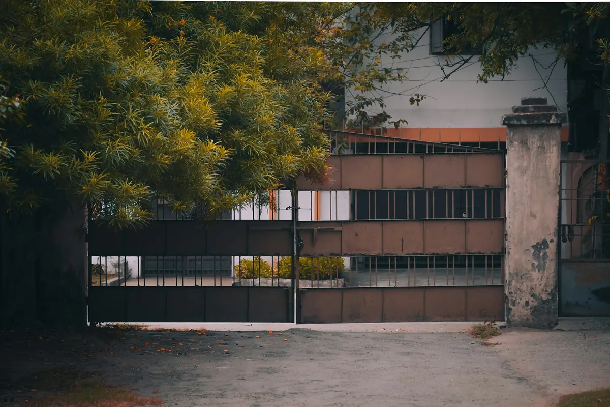 Portón corredizo oscuro de una casa con árboles detrás